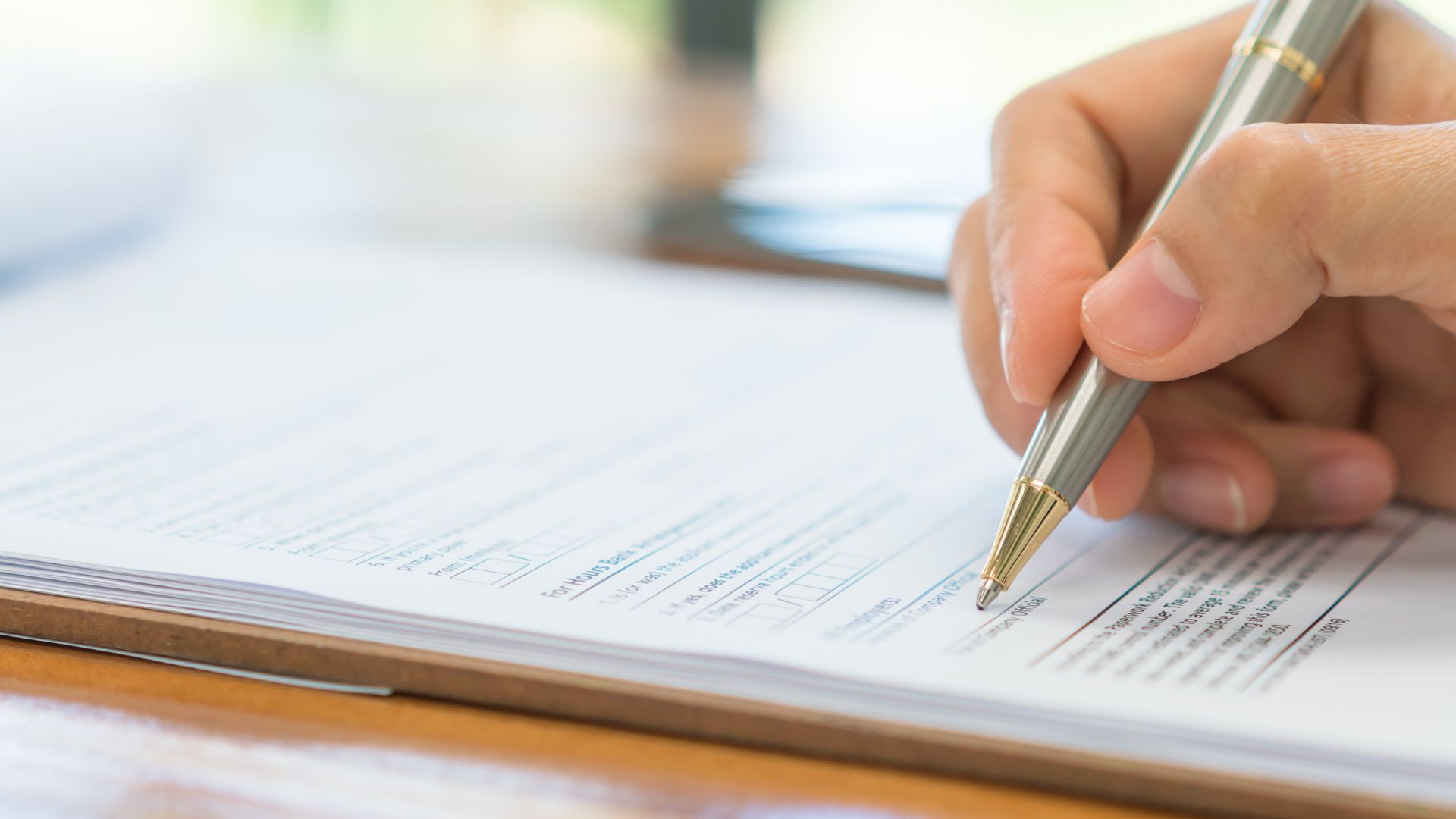 A hand holding a pen writes on a document placed on a clipboard.
